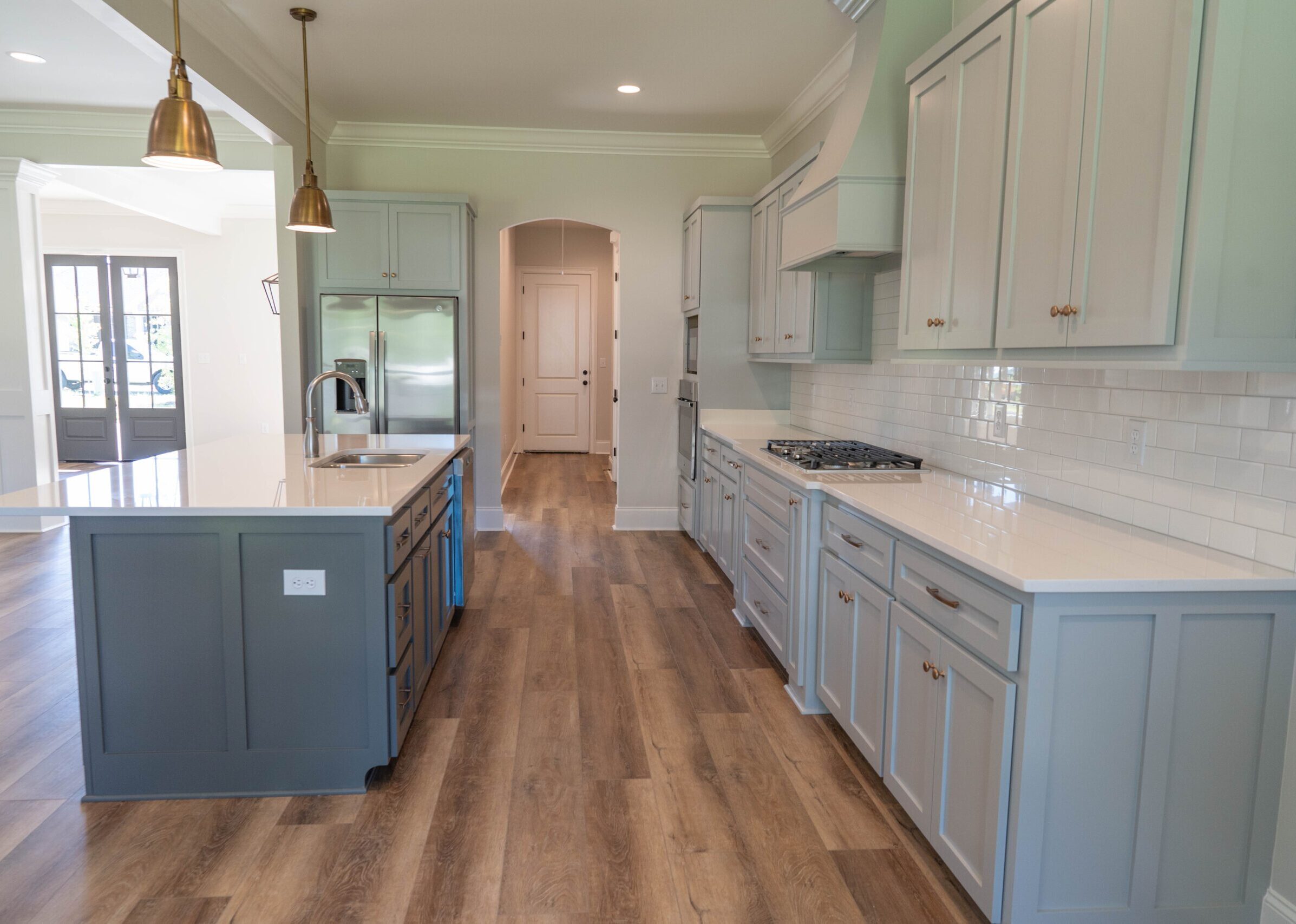 Custom kitchen with gray shaker cabinets, white quartz countertops, a contrasting island, subway tile backsplash, custom range hood, and brass pendant lights at 12521 Westwood Place in Florence Gardens, Gulfport, Mississippi.
