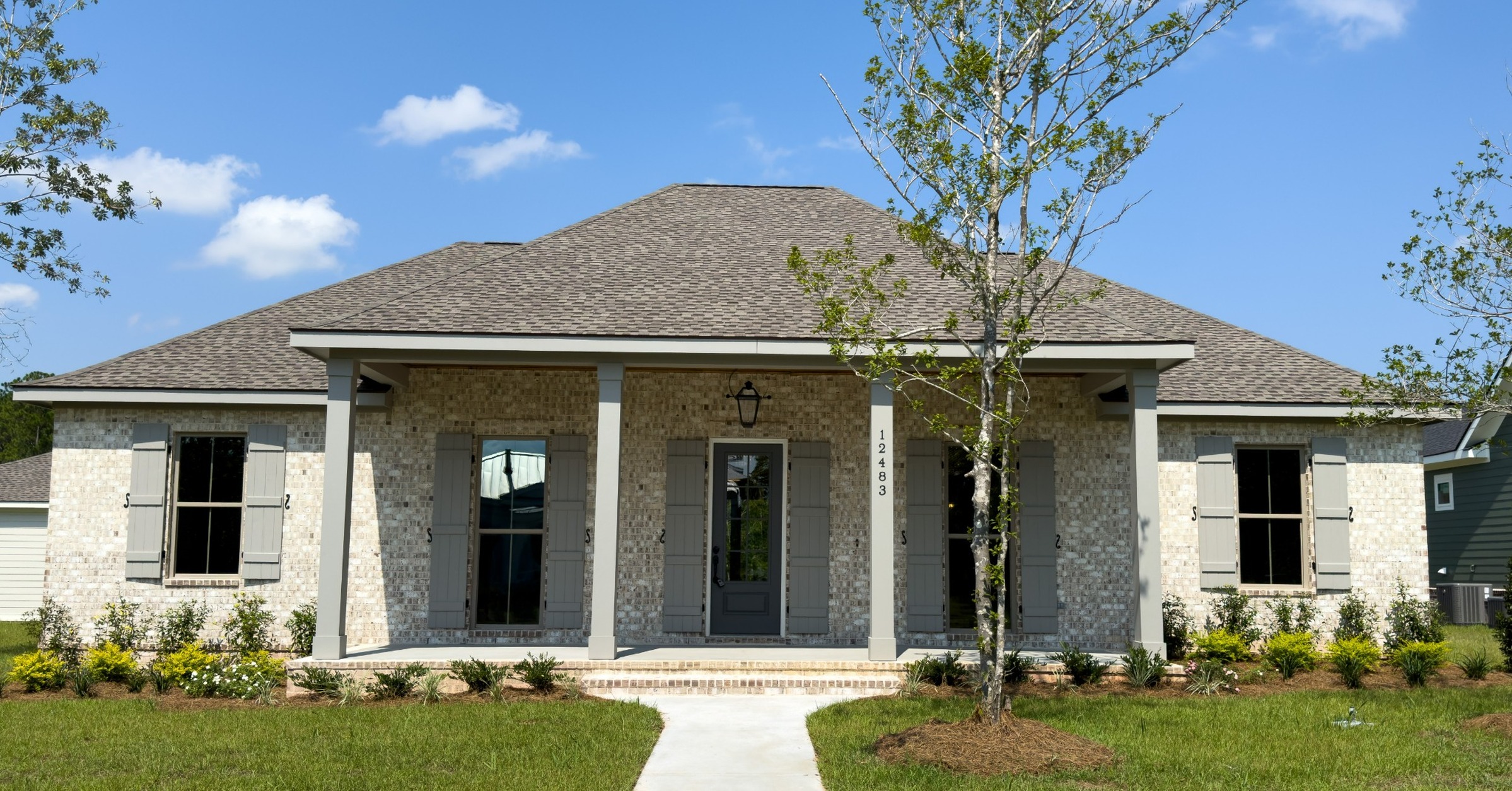Front exterior of the Cypress custom home with light brick, gray shutters, covered porch, and landscaped yard at 12483 Alphabet Road in Florence Gardens, Gulfport, Mississippi 39503.