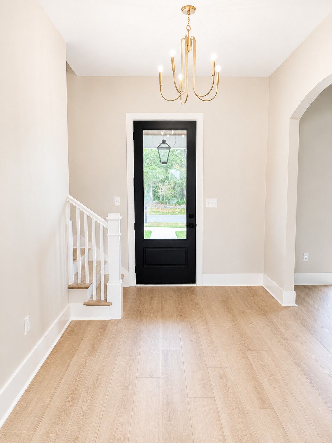 Bright custom home foyer with a black glass front door, light wood flooring, staircase, and brass chandelier in Florence Gardens, Gulfport, Mississippi.
