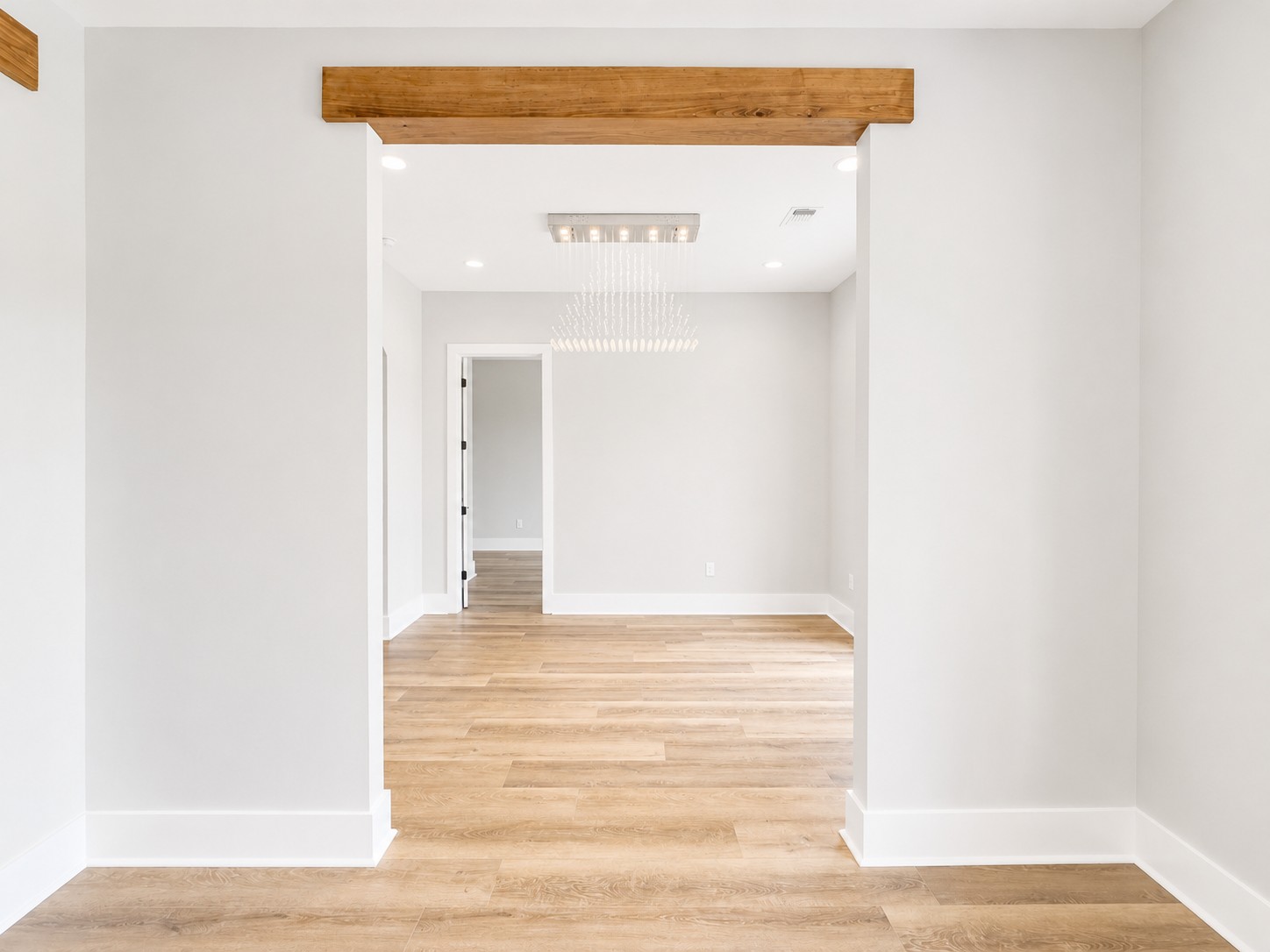 Foyer with a cypress wrapped beam, modern crystal chandelier, neutral walls, and wood-look flooring in the Cypress custom home at 12483 Alphabet Road in Florence Gardens, Gulfport, Mississippi 39503.