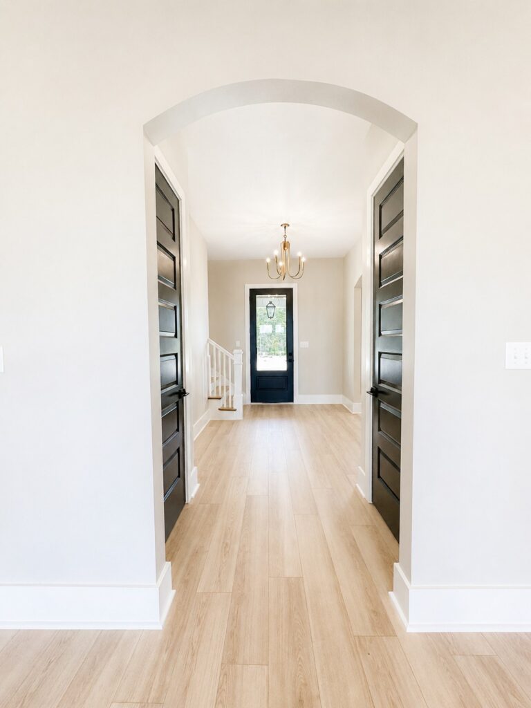 Interior view from the living area into a bright foyer with an arched opening, black interior doors, glass front door, chandelier, and light wood flooring at 12487 Alphabet Road in Florence Gardens, Gulfport, Mississippi 39503.