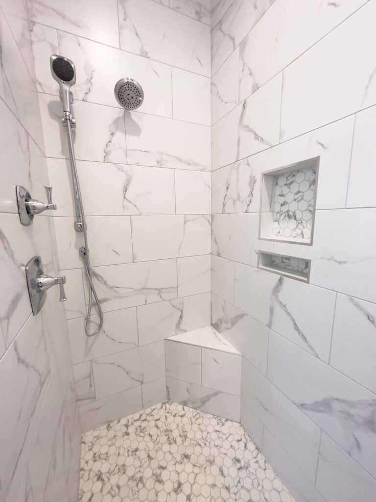 Custom tile shower to the ceiling with handheld shower head in the primary bathroom of the Cypress custom home at 12483 Alphabet Road, Florence Gardens, Gulfport, MS 39503.