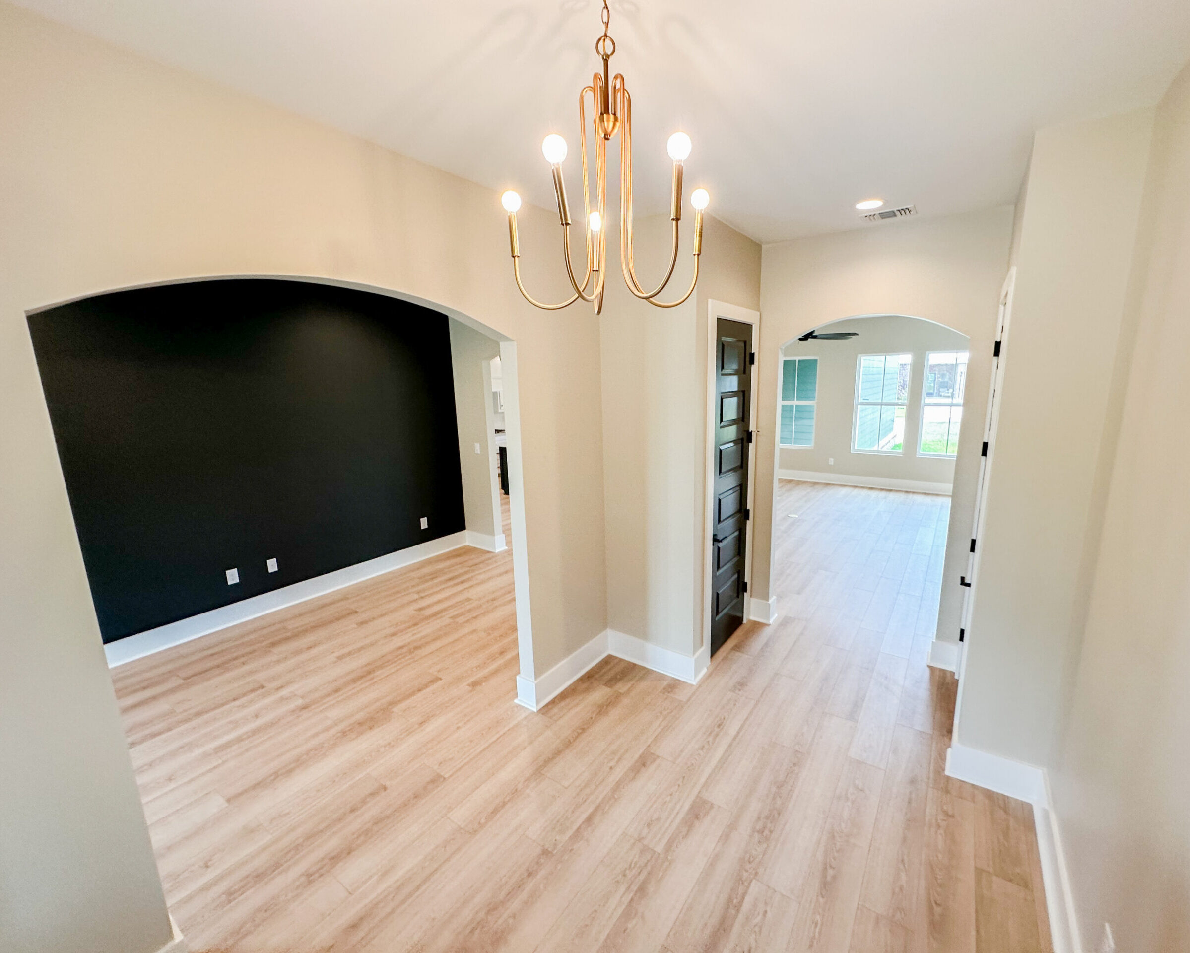 Foyer with arched openings, brass chandelier, black interior door, light wood flooring, and adjacent flex room at 12487 Alphabet Road in Florence Gardens, Gulfport, Mississippi 39503.