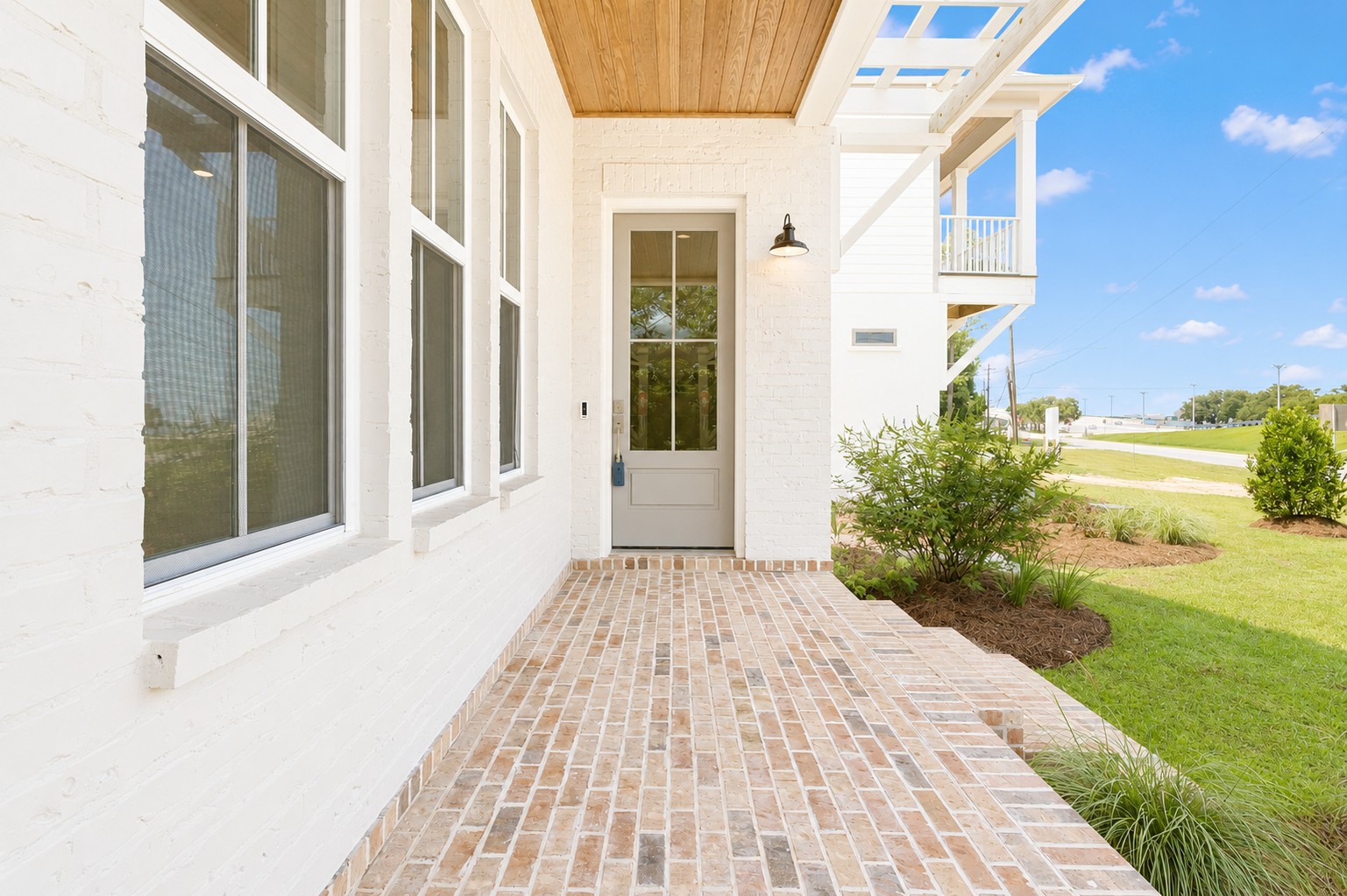 Covered front porch with brick paver flooring, white painted brick, wood ceiling, and glass entry door at 298 Porter Avenue in downtown Ocean Springs, Mississippi 39564.