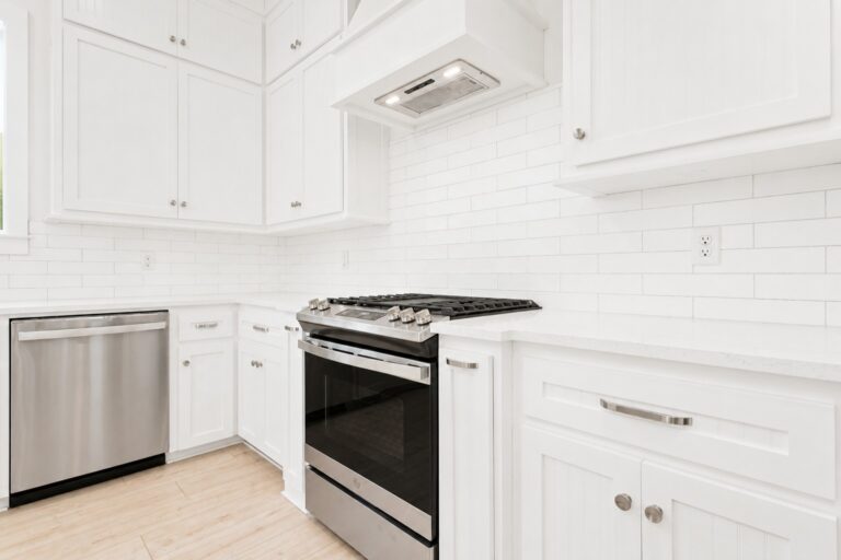 White custom kitchen with shaker-style cabinets, subway tile backsplash, stainless steel appliances, and light wood flooring at 298 Porter Avenue in downtown Ocean Springs, Mississippi 39564.