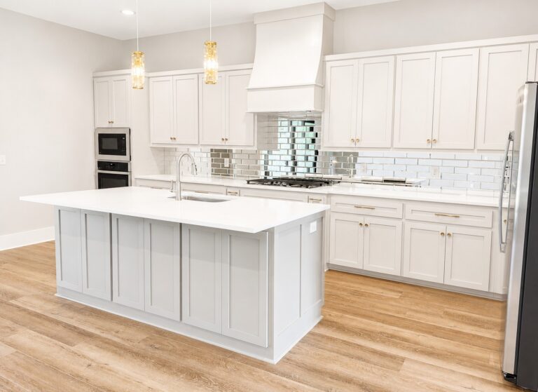 Custom kitchen with white shaker cabinets, a light gray island, white quartz countertops, mirrored subway tile backsplash, brass accents, and wood-look flooring in the Cypress home at 12483 Alphabet Road in Florence Gardens, Gulfport, Mississippi 39503