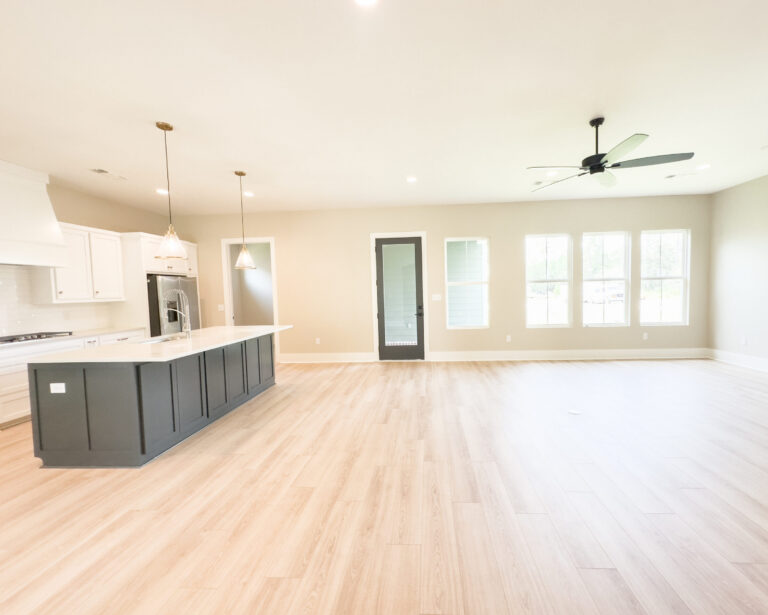 Open-concept kitchen and living room with a dark kitchen island, white cabinetry, pendant lights, light wood flooring, large windows, and a black ceiling fan at 12487 Alphabet Road in Florence Gardens, Gulfport, Mississippi 39503.