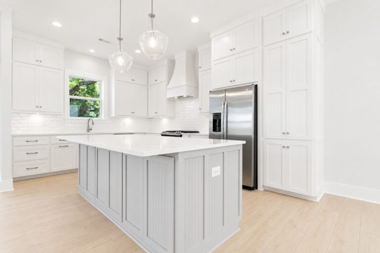 Bright custom kitchen with white beaded shaker cabinets, a gray island, white countertops, glass pendant lights, and stainless steel appliances at 298 Porter Avenue in downtown Ocean Springs, Mississippi 39564.