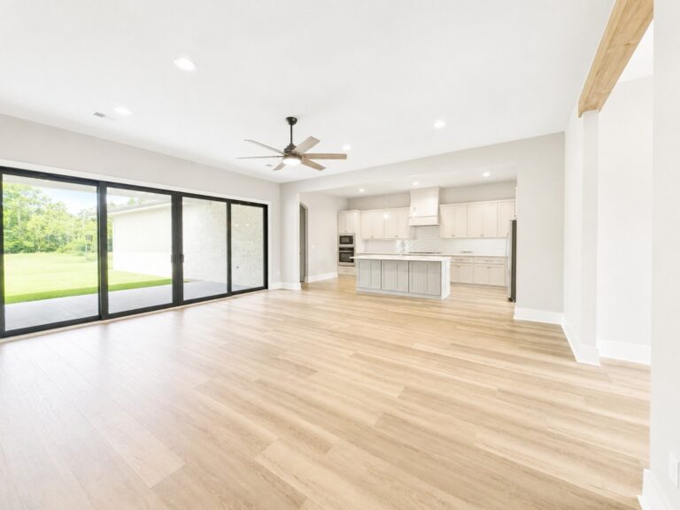 Open-concept living room and kitchen with wood-look flooring, large sliding glass doors, a cypress wrapped beam, and quartz countertops in the Cypress custom home at 12483 Alphabet Road in Florence Gardens, Gulfport, Mississippi 39503.