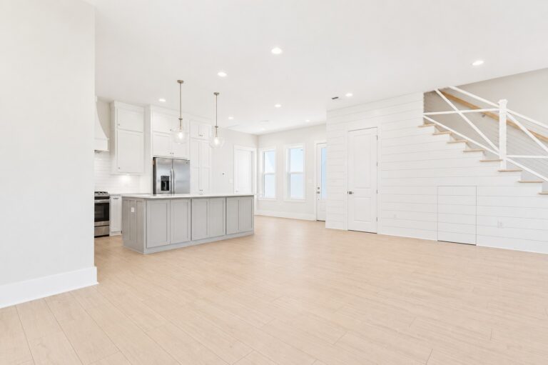 Open-concept living, kitchen, and dining area with light wood flooring, a gray kitchen island, white cabinetry, and a shiplap staircase at 298 Porter Avenue in downtown Ocean Springs, Mississippi 39564.