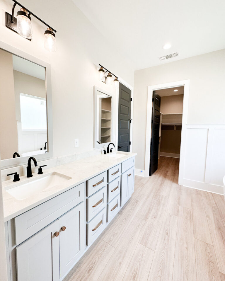 Primary bathroom with a gray double vanity, white countertops, black fixtures, framed mirrors, and light wood flooring at 12487 Alphabet Road in Florence Gardens, Gulfport, Mississippi 39503