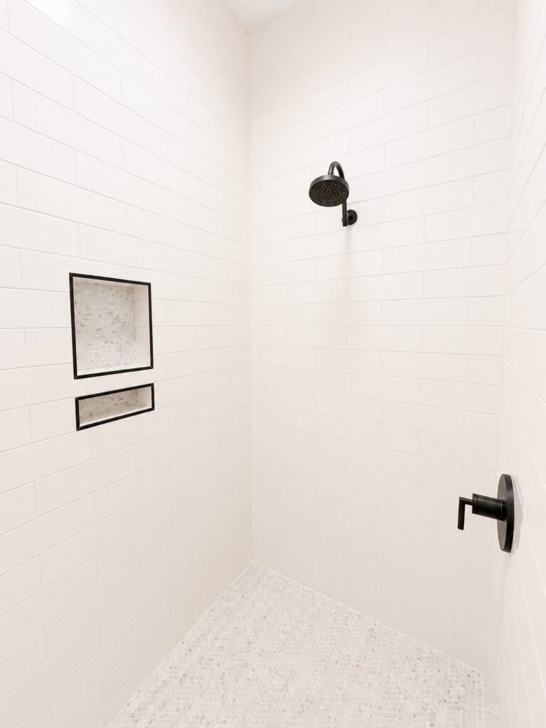 Primary bathroom shower with white subway tile, a herringbone mosaic floor, built-in niches, and matte black fixtures at 12487 Alphabet Road in Florence Gardens, Gulfport, Mississippi 39503.