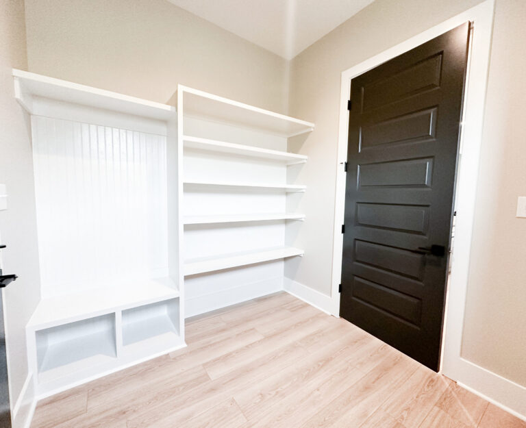 Custom mudroom with built-in white shelving, storage bench, black interior door, and light wood flooring at 12487 Alphabet Road in Florence Gardens, Gulfport, Mississippi 39503.
