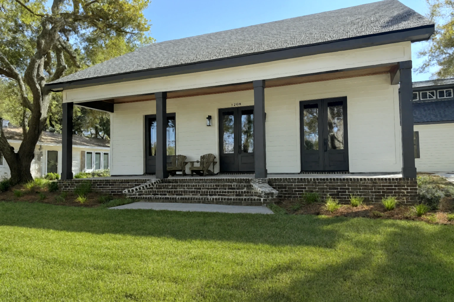 Covered porch with black doors and windows, brick steps, and outdoor seating at the Schmidt Home in Ocean Springs by BW Artisan Homes.
