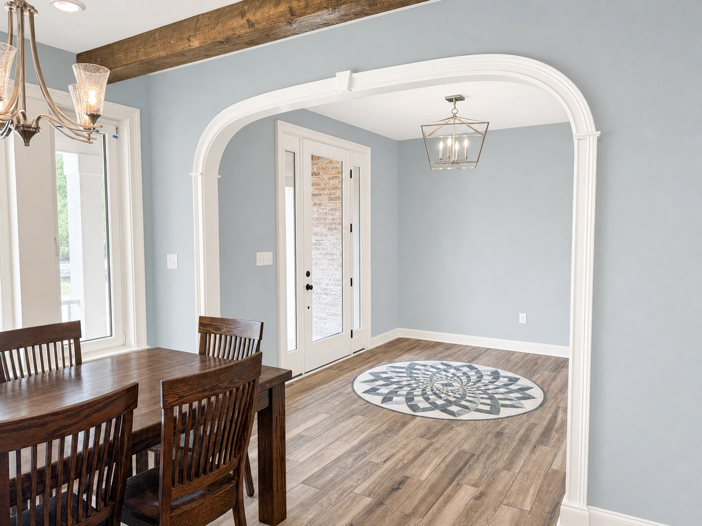 Dining area with dark wood chairs and table, arched doorway leading to an entry with glass door and sidelights, decorative ceiling beam, and patterned floor medallion in Vancleave by BW Artisan Homes.
