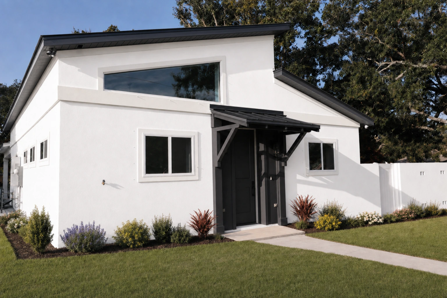 Front view of a modern white stucco home with black windows and door under a standing seam metal roof by BW Artisan Homes in Long Beach, Mississippi.