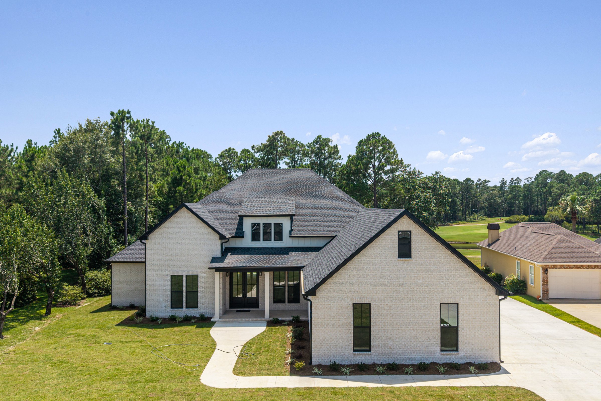 Front view of a white brick home with black windows and a covered porch by BW Artisan Homes in Gulfport, MS, surrounded by a lush green lawn and trees.