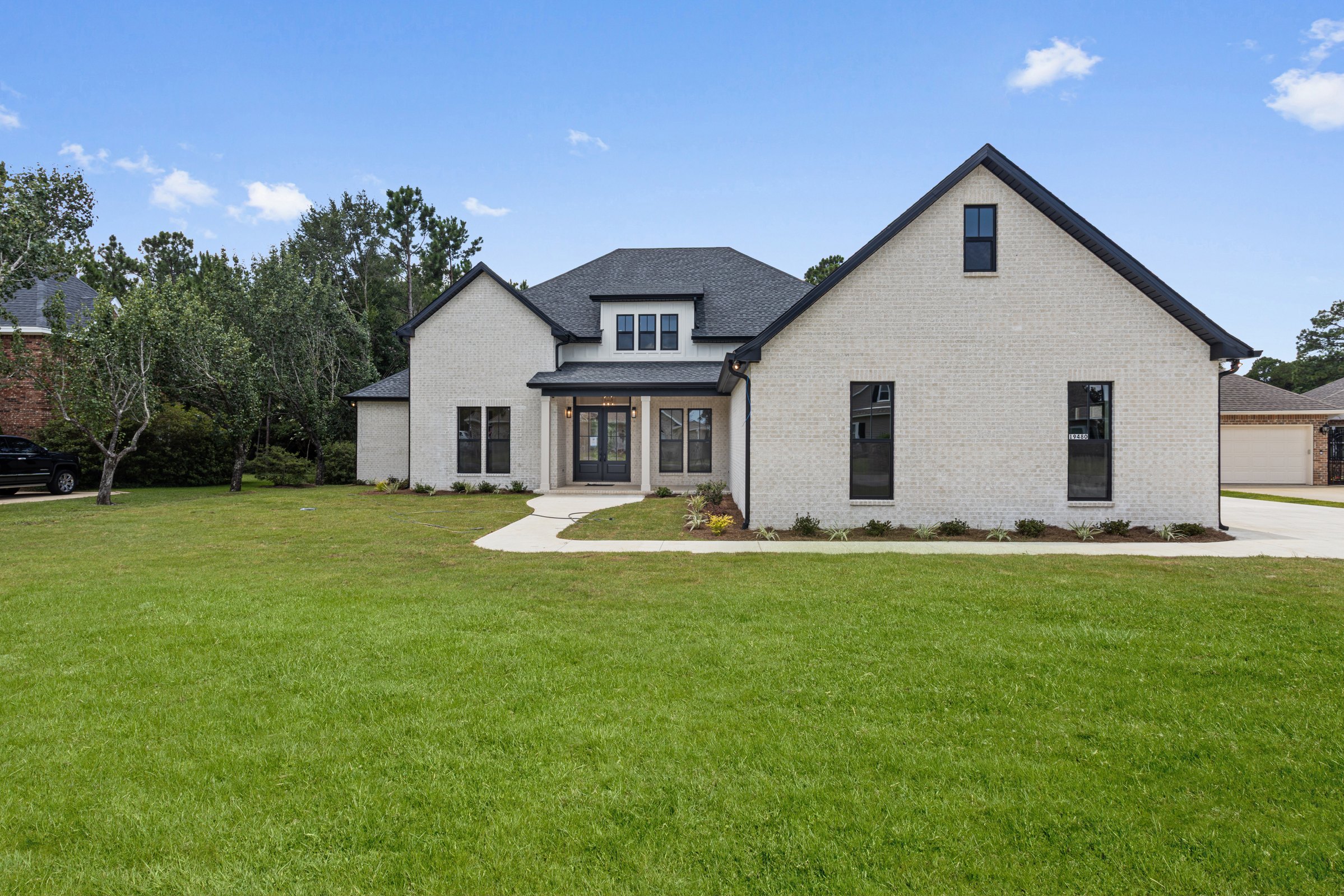 Front view of a modern home in Gulfport with white brick, black windows, and a covered porch by BW Artisan Homes.