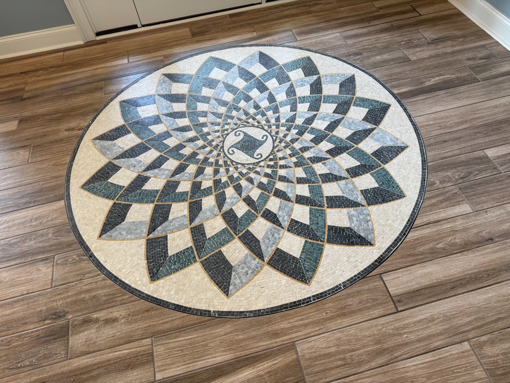 Decorative circular tile medallion set in wood-look tile flooring in a foyer with natural light, built by BW Artisan Homes in Vancleave MS.