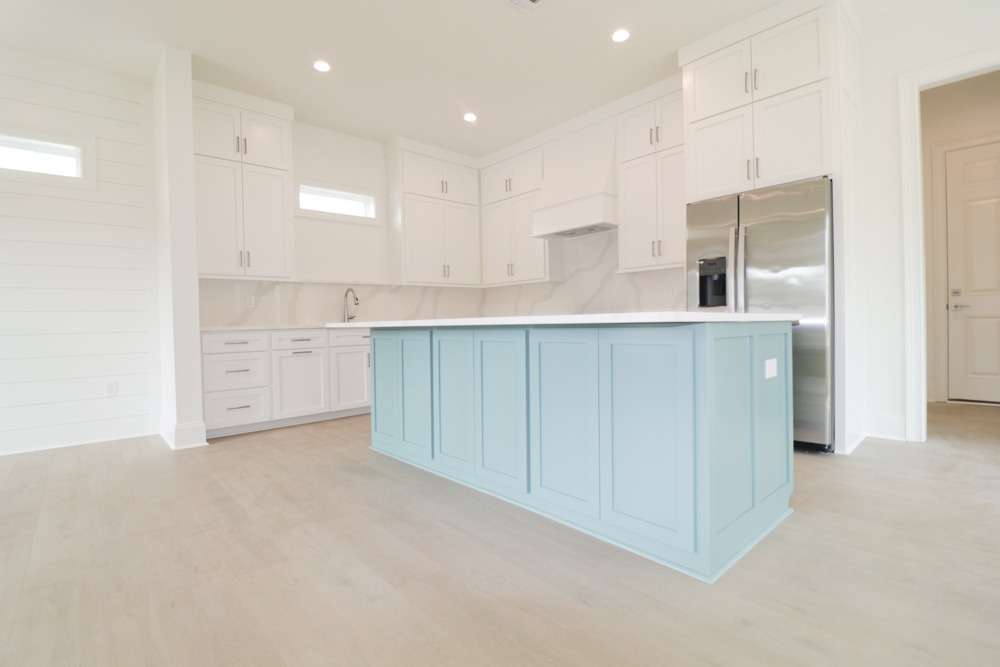 Bright kitchen with custom white cabinetry, blue kitchen island, quartz countertops, and stainless steel refrigerator in BW Artisan Homes Porter III Ocean Springs.