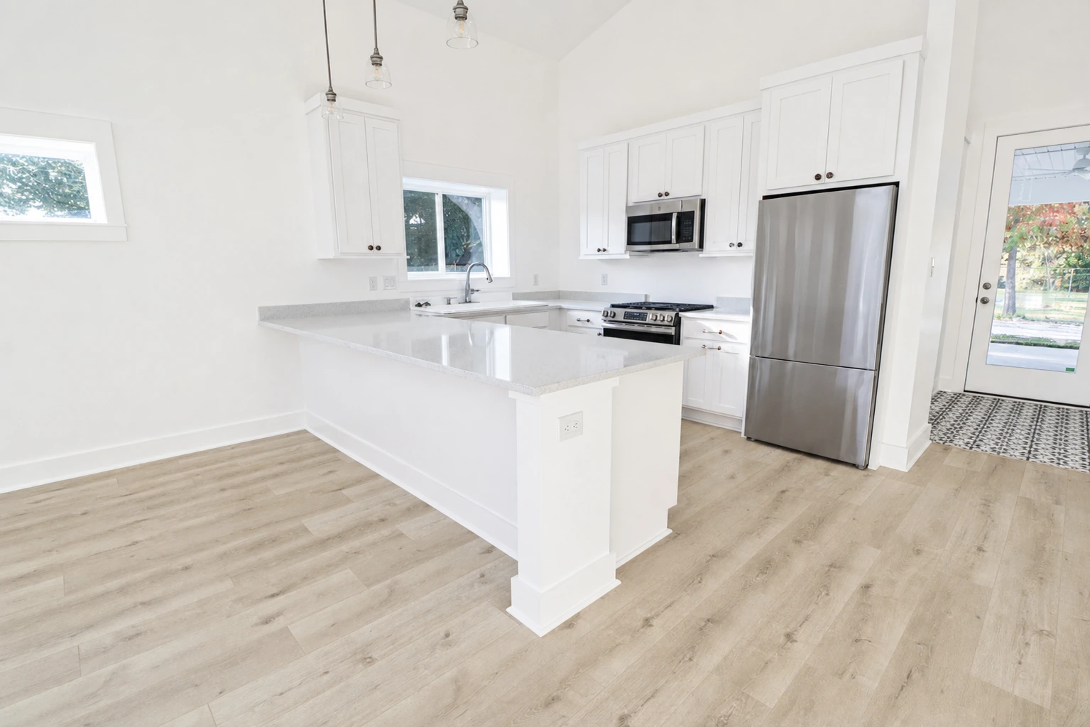 Bright kitchen with white custom cabinetry, quartz countertops, stainless steel appliances, and white oak flooring by BW Artisan Homes in Long Beach, MS.