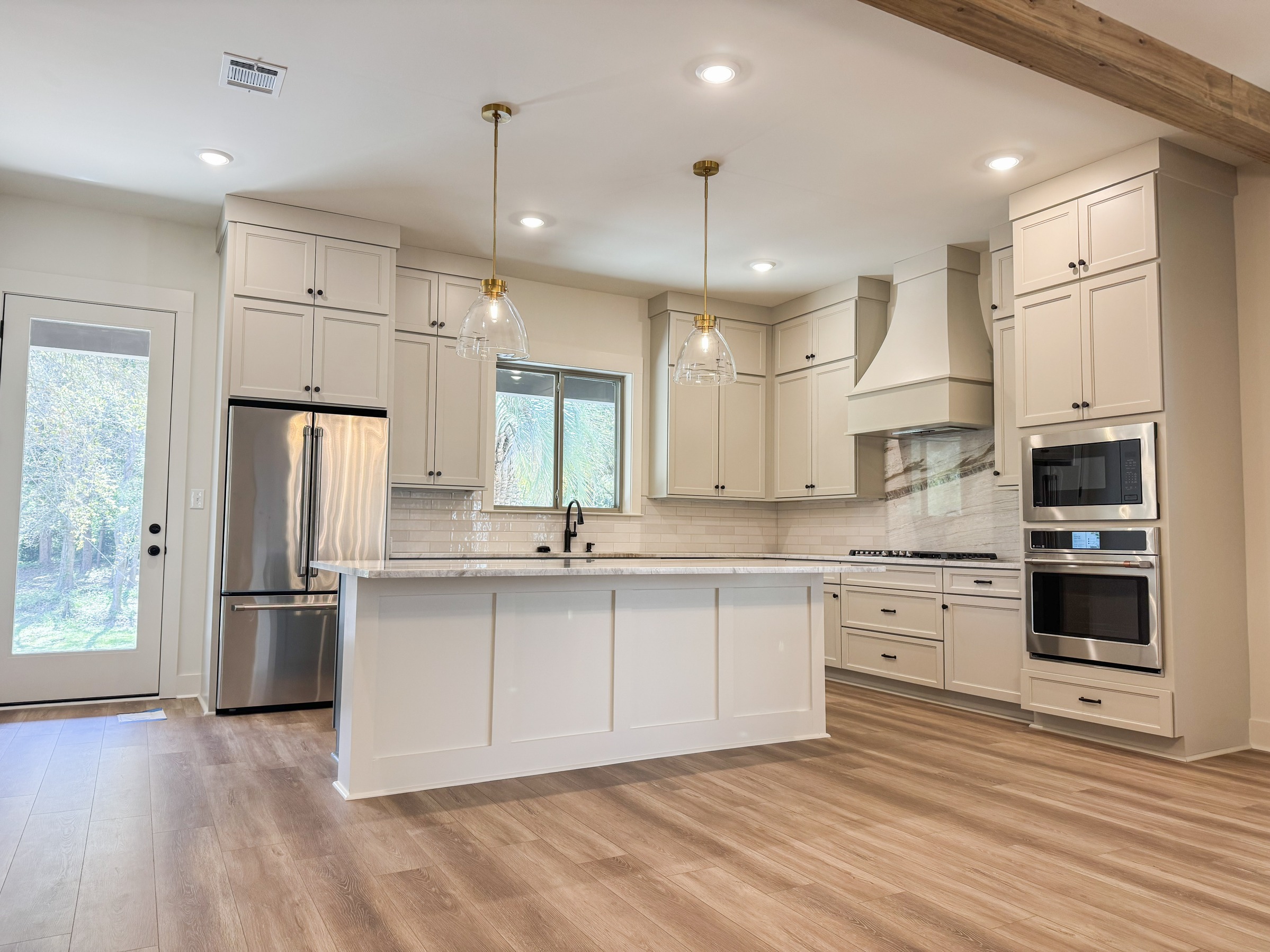 Bright kitchen with white custom cabinetry, quartz countertops, pendant lighting, and stainless steel appliances by BW Artisan Homes in Ocean Springs.
