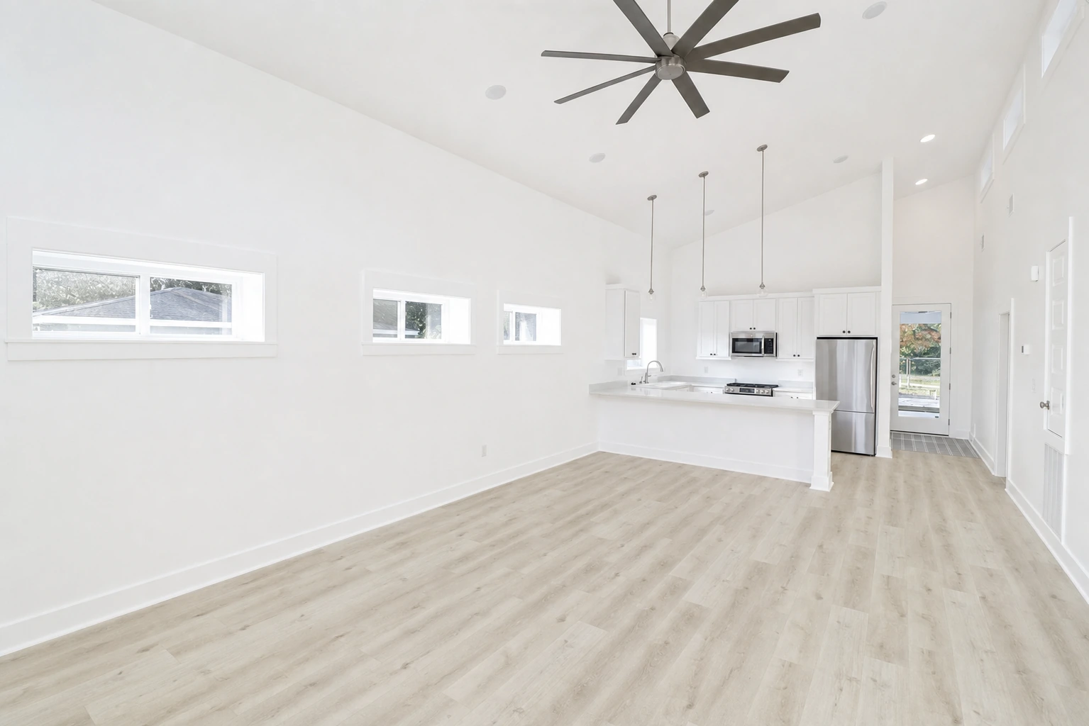 Bright kitchen and living area with white cabinetry, quartz countertops, and large ceiling fan by BW Artisan Homes in Long Beach, Mississippi.