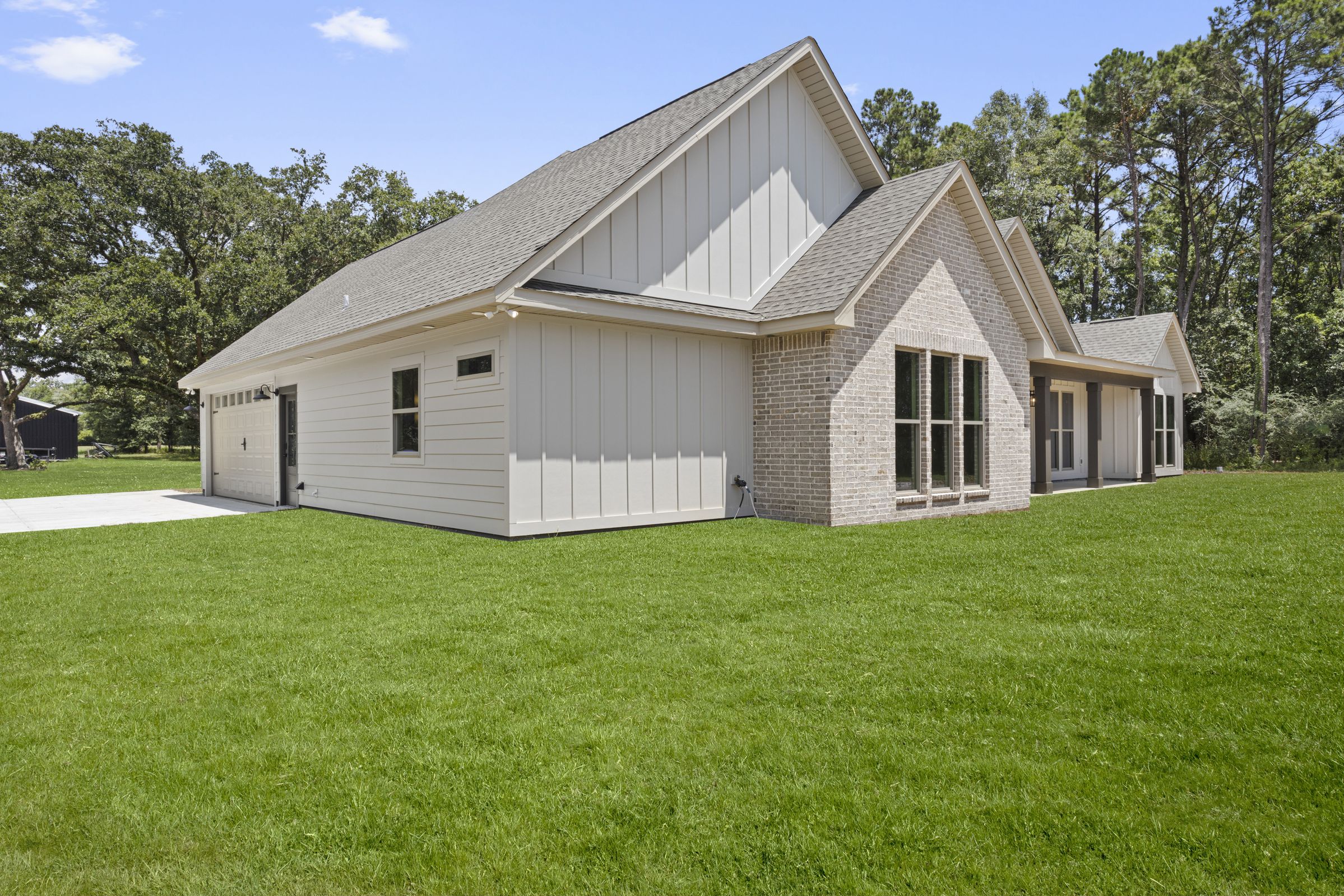 Light-colored custom home exterior in Pass Christian with brick accent wall, board and batten siding, black windows, and attached garage by BW Artisan Homes.