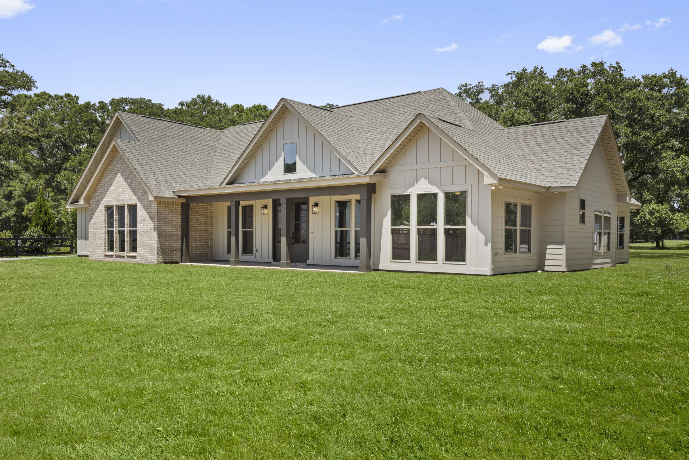 Bright exterior of the Gilmore Residence showing a covered porch, white siding, and brick accent wall surrounded by green lawn, by BW Artisan Homes in Pass Christian.