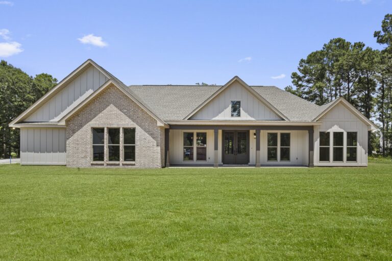 Front exterior view of Gilmore Residence by BW Artisan Homes in Pass Christian, MS showing brick facade, covered porch, and black windows under a clear sky.