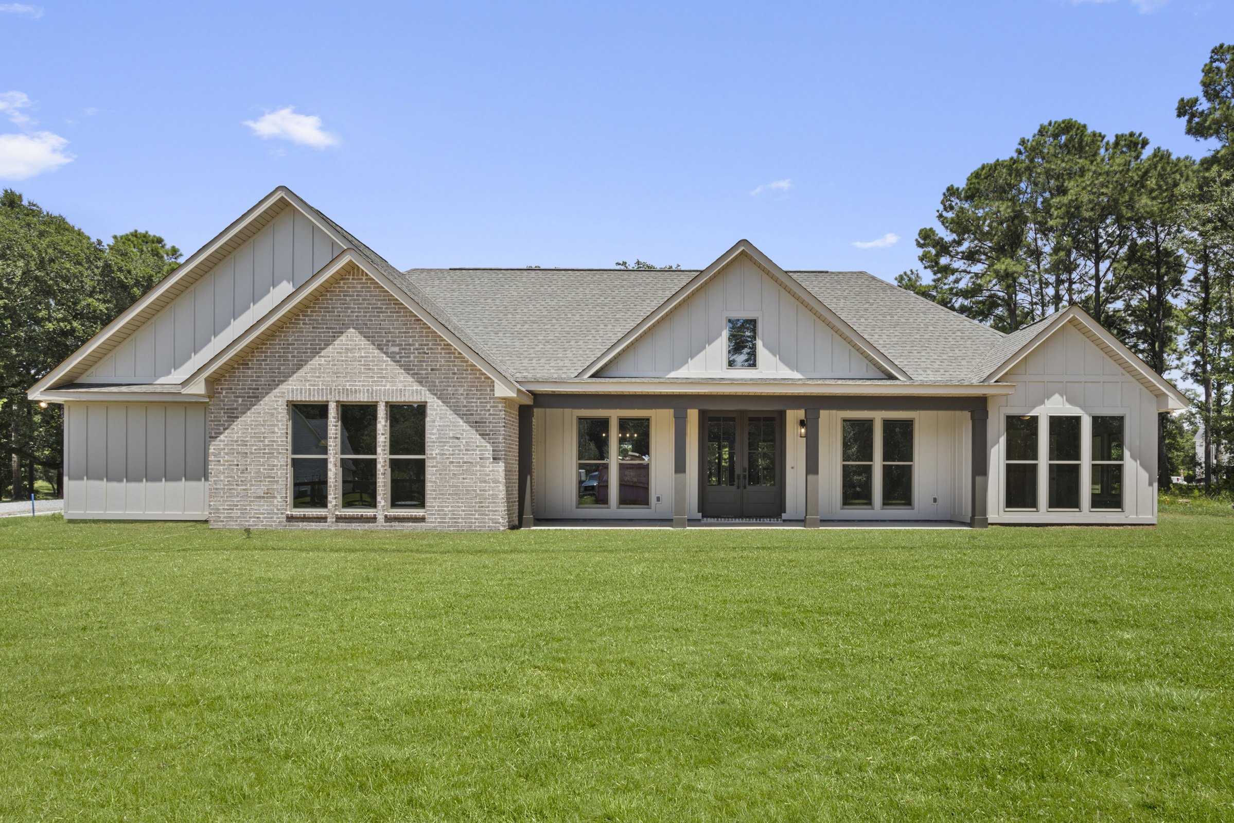 Front exterior view of Gilmore Residence by BW Artisan Homes in Pass Christian, MS showing brick facade, covered porch, and black windows under a clear sky.
