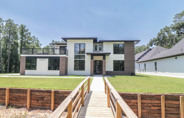 Front exterior of a modern custom home by BW Artisan Homes in Gulfport, MS featuring large black windows, composite shiplap siding, and a second-story deck.