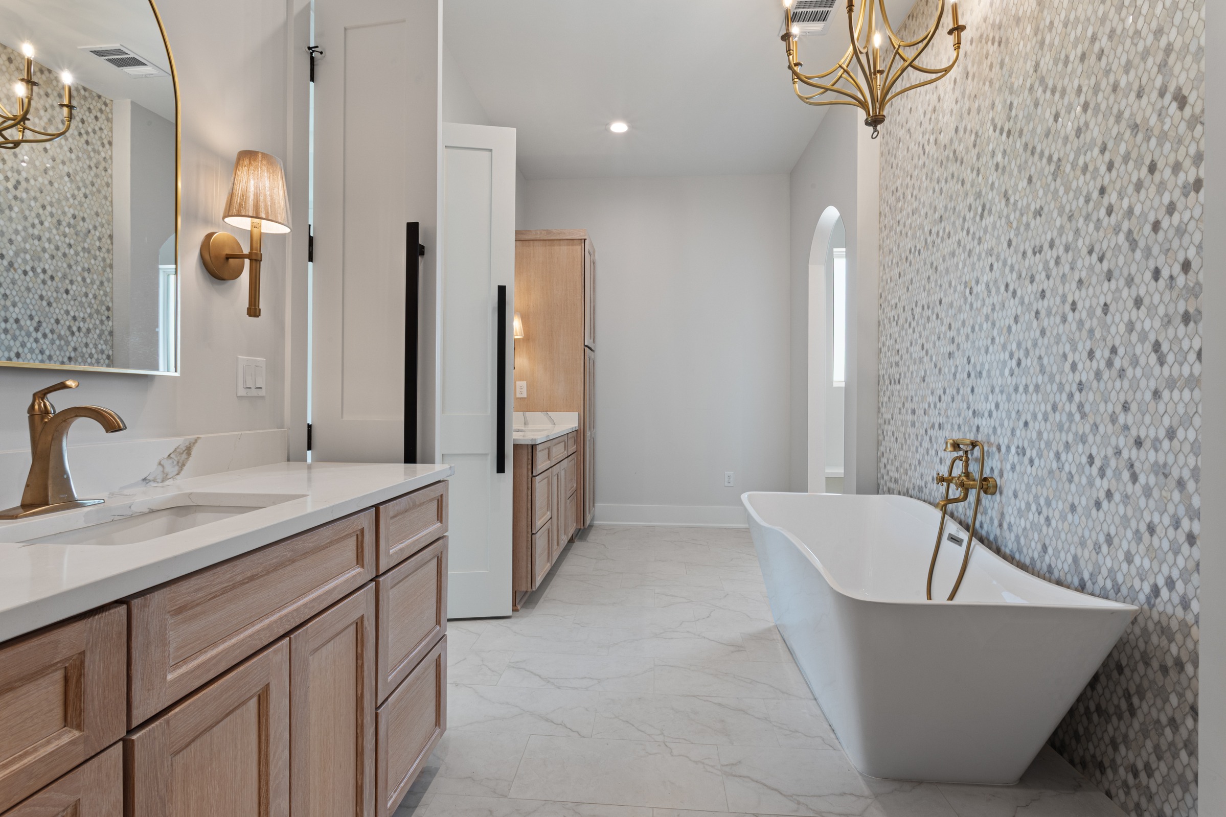 Spacious bathroom in the Fore Family home by BW Artisan Homes in Gulfport, MS, featuring a white freestanding tub, custom oak cabinetry, and a tiled accent wall.