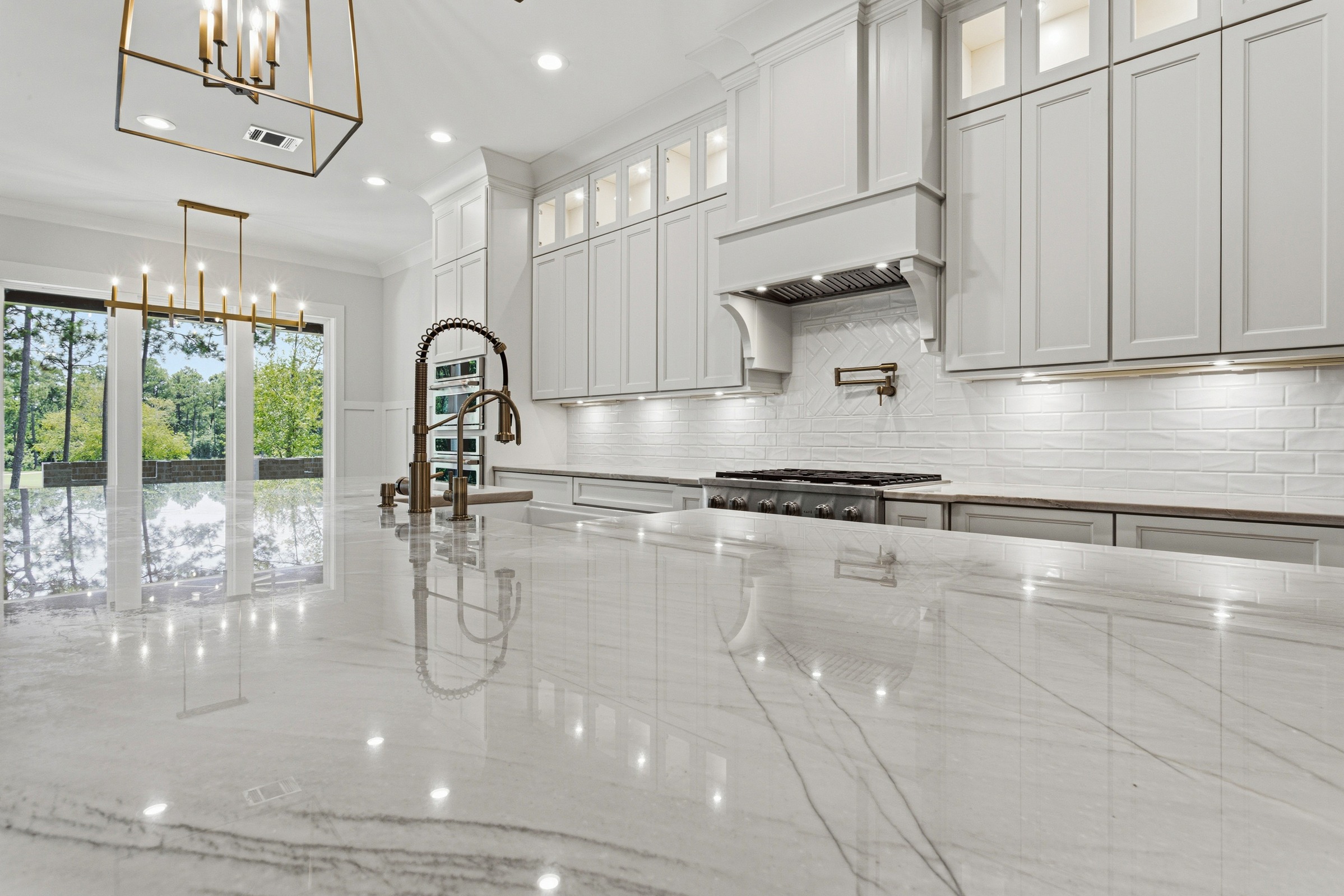 A bright kitchen with white custom cabinetry, quartz countertops, black windows, and gold fixtures by BW Artisan Homes in Gulfport, MS.