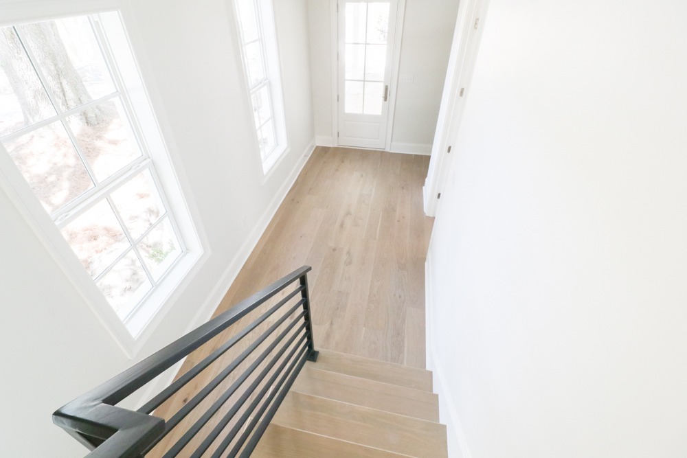 Bright stairwell with white oak flooring and black window frames, showcasing natural light in a BW Artisan Homes custom in Ocean Springs, Mississippi.